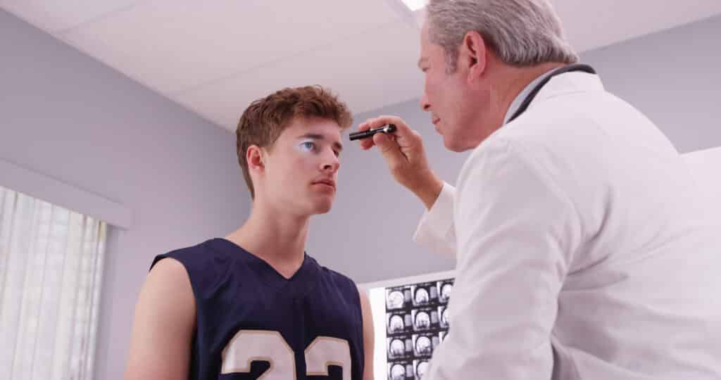 Senior medical doctor checking basketball player's eyes with flashlight. SRC Management